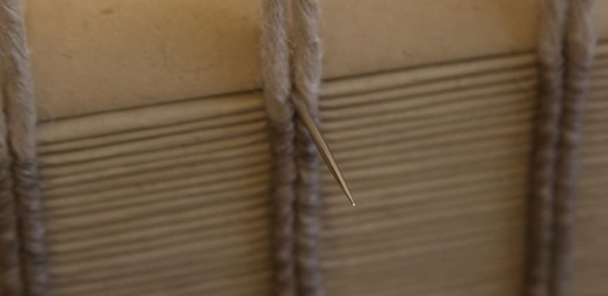 To form the herringbone stitch, the needle exits between the paired cords…